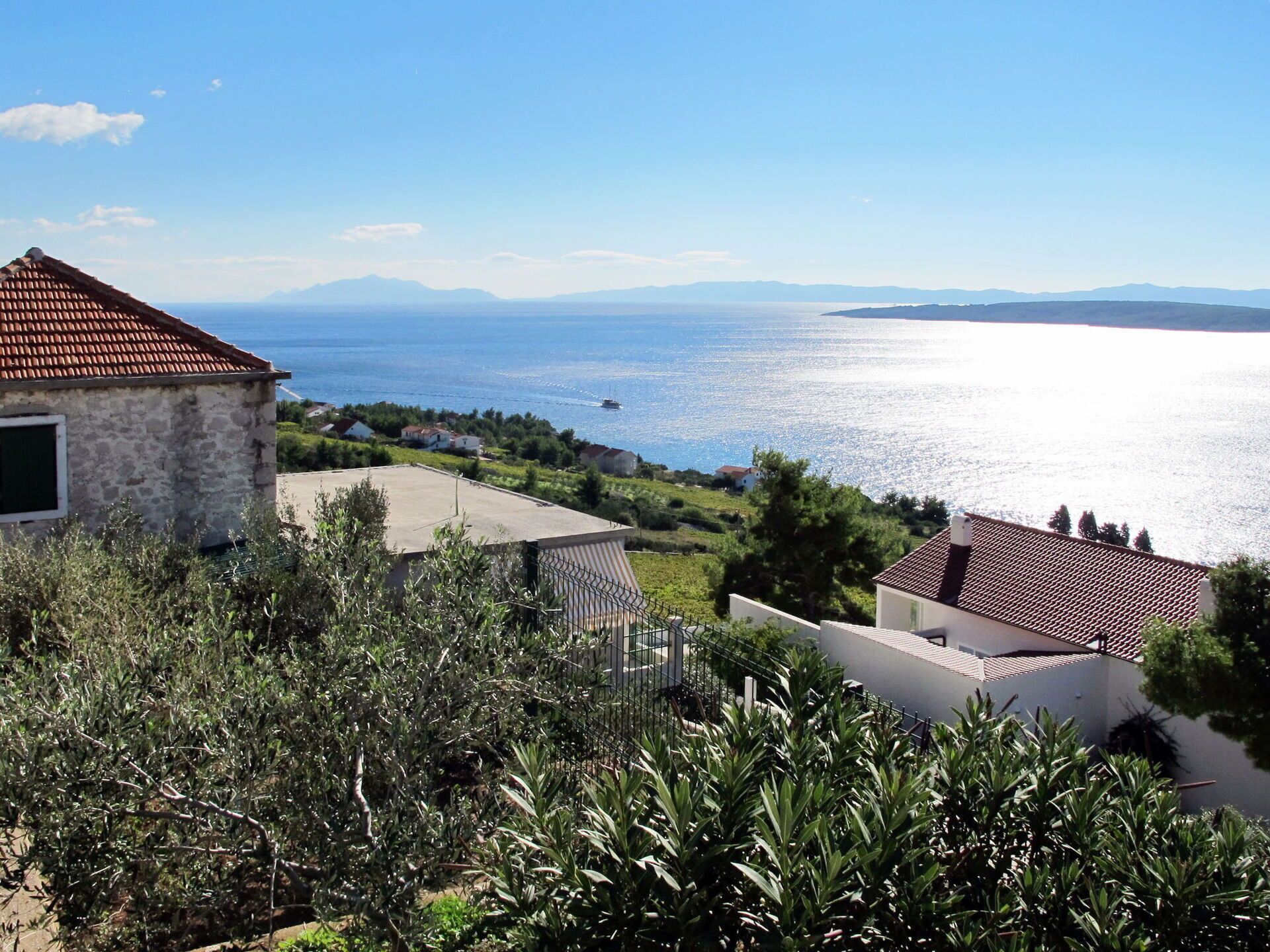 A coastal property with a stone building, a fenced garden, and a view of the sea and distant mountains.