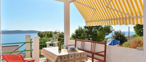 A balcony with a table and chairs, a striped awning, and a view of the sea.