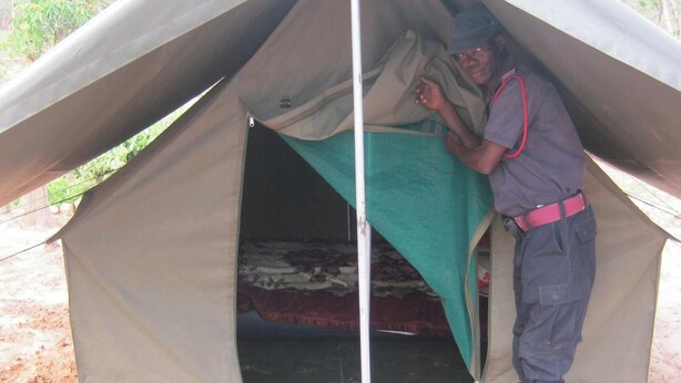 A tent with a bed inside, a person standing by the entrance, and a small vehicle parked outside. - Lochinvar Safari Lodge (Lochinvar National Park)