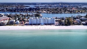 Un hotel frente al mar con varios pisos, una playa en primer plano y un puerto deportivo al fondo.