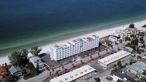 Un hotel costero con una hilera de edificios blancos, un estacionamiento y una playa al fondo.