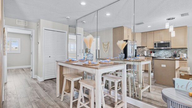 Cocina moderna con una isla central, taburetes de madera y un espejo grande que refleja el ambiente.