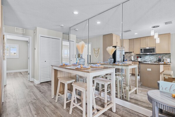 A modern kitchen with a central island, wooden stools, and a large mirror reflecting the space.
