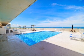 Ein Pool mit Blick auf den Ozean, umgeben von Liegestühlen und Palmen.