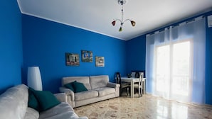 A living room with a blue wall, a beige sofa, a dining table with chairs, and a chandelier.