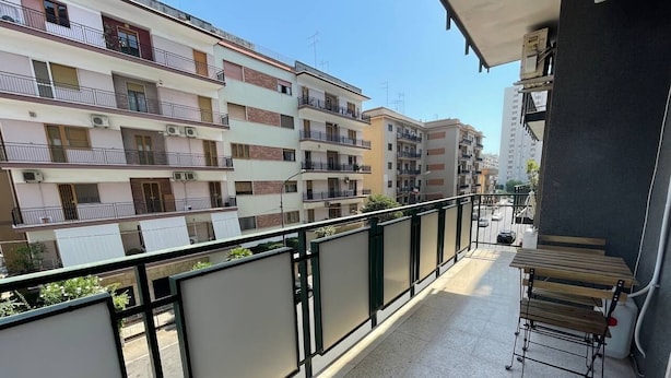 A balcony with a wooden table and chairs, a view of neighboring buildings, and a tiled floor.
