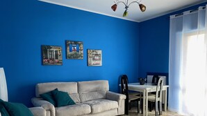 A living room with a blue wall, a beige sofa, a dining table with chairs, and a ceiling fan.