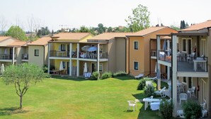 Un edificio residencial de varios pisos con balcones, mobiliario exterior y un césped bien cuidado.