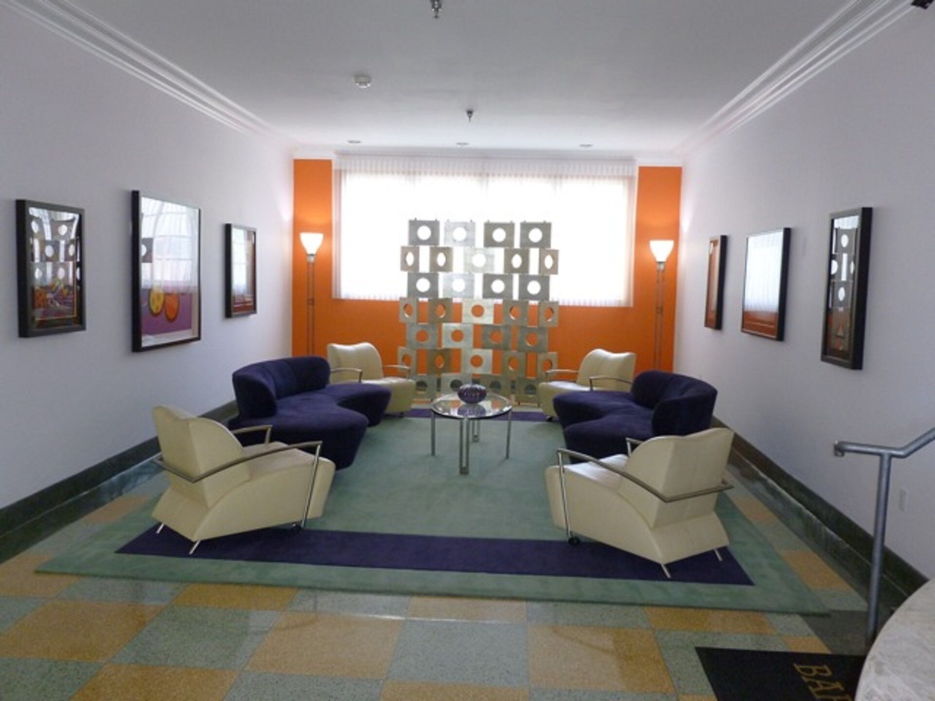 Un hall d’entrée avec un sol à carreaux, un espace détente avec des fauteuils, une table basse et un mur décoratif orné de motifs géométriques.