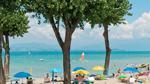 A beach with people sunbathing, swimming, and sailing. - Beautiful apartment in villa for 4 people with A/C, WIFI, pool, TV and terrace (Sirmione)