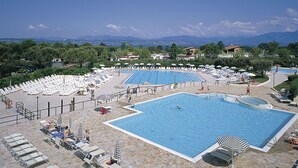 A large outdoor swimming pool with multiple lanes, surrounded by lounge chairs and umbrellas, set against a backdrop of mountains and a clear sky. - Beautiful apartment in villa for 4 people with A/C, WIFI, pool, TV and terrace (Sirmione)