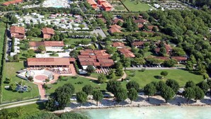 An aerial view of a coastal resort with multiple bungalow-style buildings, a central communal area with outdoor seating, and a beach area. - Beautiful apartment in villa for 4 people with A/C, WIFI, pool, TV and terrace (Sirmione)