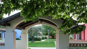 An arched entrance with a stone pathway leading to a green lawn and a building in the background. - Beautiful apartment in villa for 4 people with A/C, WIFI, pool, TV and terrace (Sirmione)
