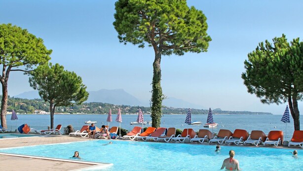 Ein Poolbereich mit Liegestühlen und Sonnenschirmen, mit Blick auf das Meer und Berge im Hintergrund.