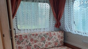 Tunnelmallinen sisustus, jossa on kukkapainokuosilla varustettu penkki, pitsiverhot ja laattalattia.