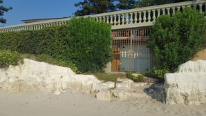 Un edificio costero con balcón, rodeado de abundante vegetación y un litoral rocoso.