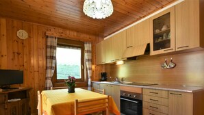 A wooden interior with a dining table, chairs, a television, a kitchen with wooden cabinets, a sink, and an oven. - Lovely apartment for 4 guests with WIFI, TV and terrace (Baite)