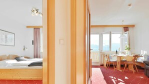 Una camera d'hotel con un letto, un'area pranzo con tavolo e sedie, e vista sulle montagne attraverso ampie finestre.