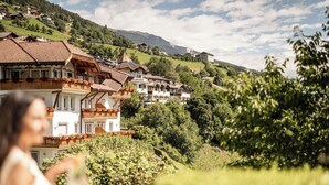A traditional chalet-style building with multiple balconies, surrounded by lush greenery and set against a backdrop of rolling hills. - Beautiful apartment for 4 guests with WIFI, pool, TV, balcony and pets allowed (Villandro)