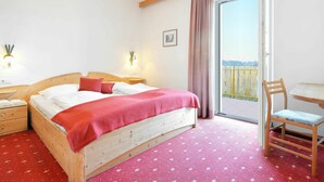A bedroom with a wooden bed, a red blanket, a nightstand, a bedside table, a chair, a table, a window with a view, and a picture on the wall. - Beautiful apartment for 4 guests with WIFI, pool, TV, balcony and pets allowed (Villandro)