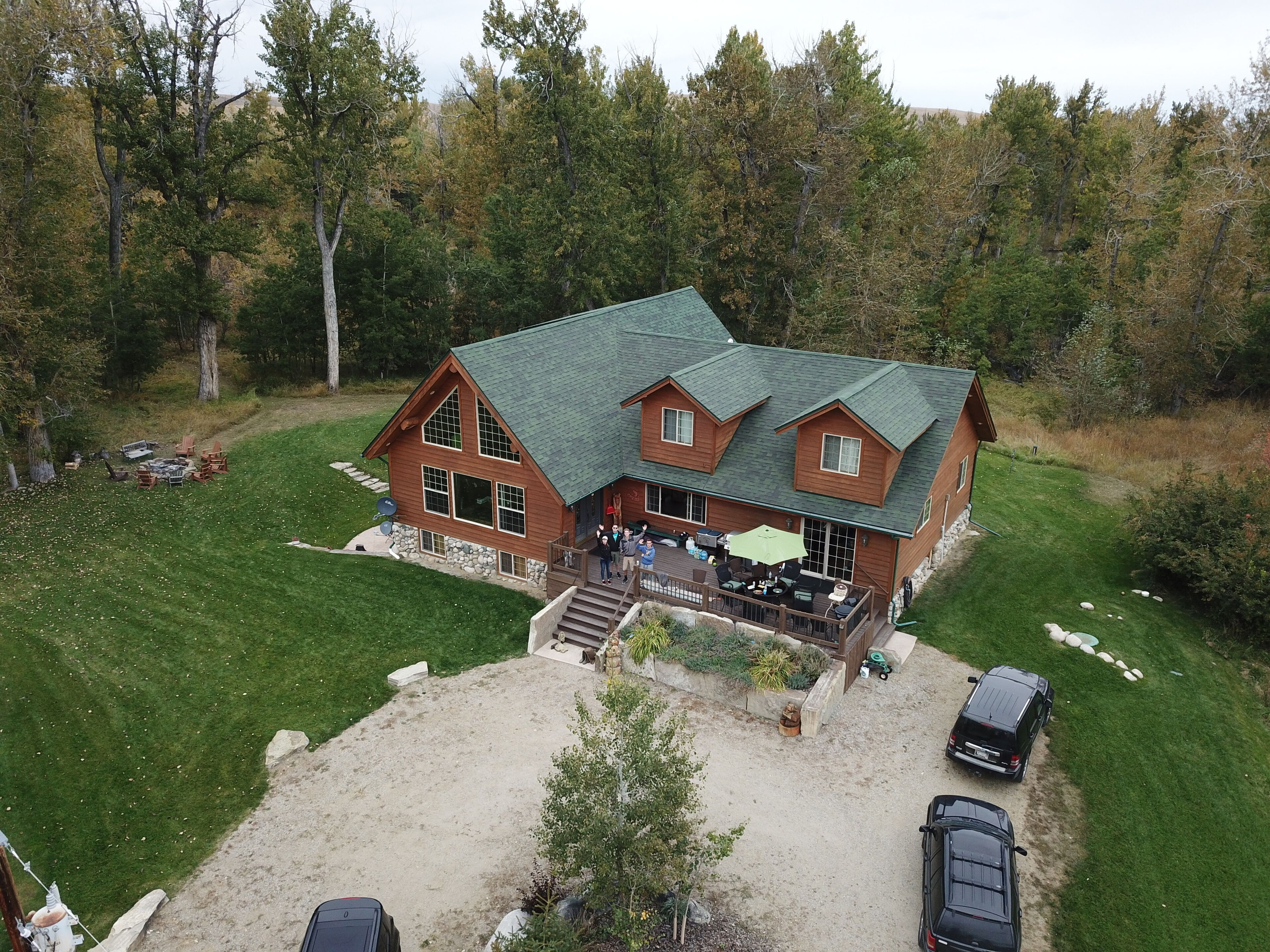 A large, two-story log cabin with a green roof, surrounded by a well-maintained lawn and a forested area.