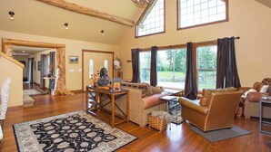 A spacious living room with a high ceiling, large windows, a wooden floor, and a cozy seating area. - Luxury Riverfront Beartooth Mountain Lodge - Private Retreat! Visit Yellowstone (Roscoe)