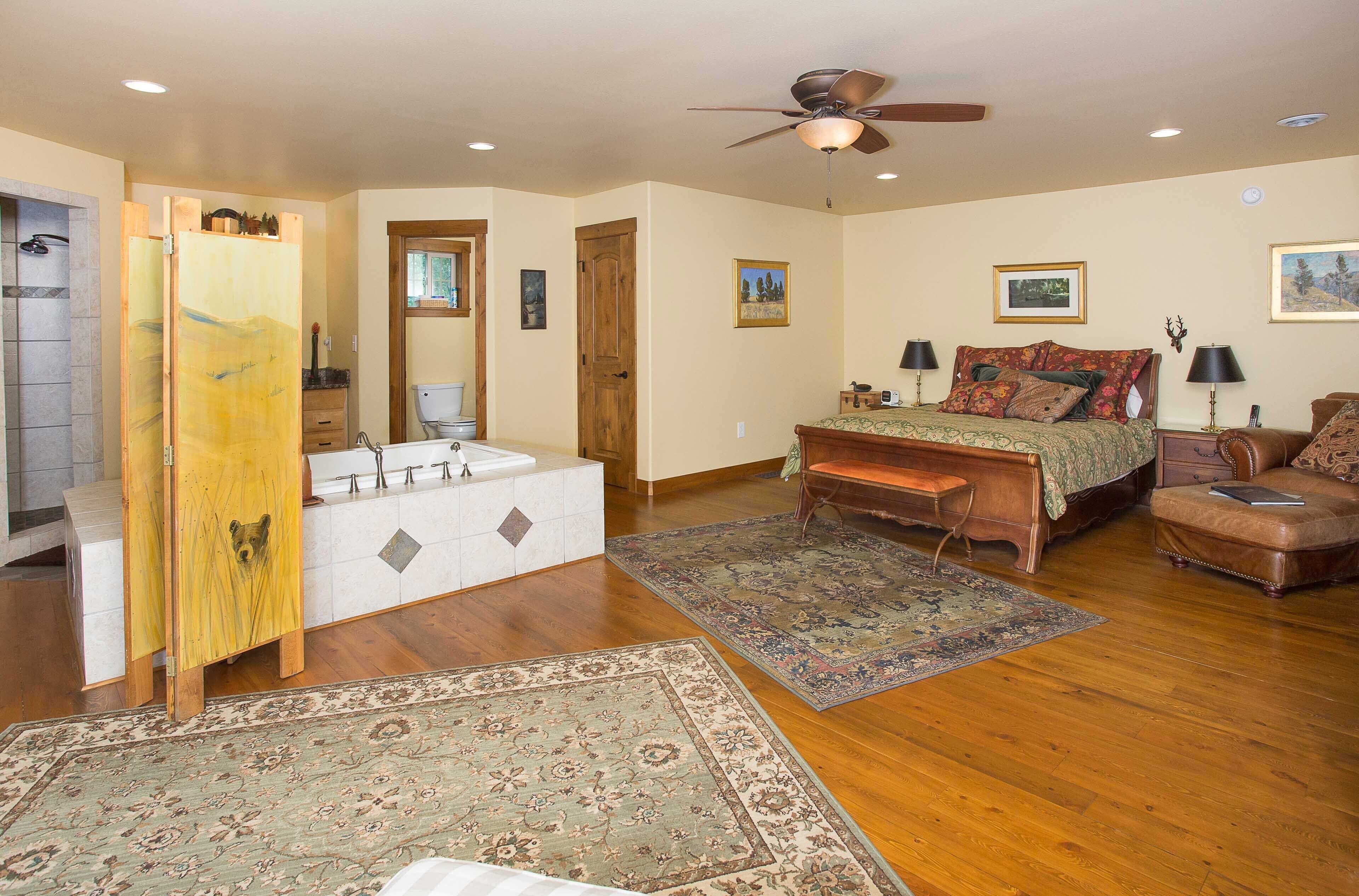A bedroom with a wooden bed, a bench, a dresser, a ceiling fan, and a large rug.