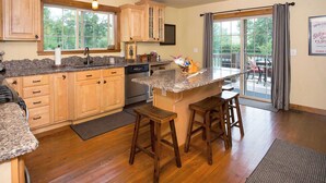 A kitchen with wooden cabinets, granite countertops, and a large window. There are two wooden stools and a small island with stools. - Luxury Riverfront Beartooth Mountain Lodge - Private Retreat! Visit Yellowstone (Roscoe)