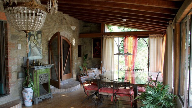Une pièce rustique avec une cheminée en pierre, des poutres apparentes, une table à manger avec des chaises et une grande fenêtre avec des rideaux.
