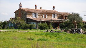 Une maison de campagne en pierre, avec un toit en tuiles, plusieurs cheminées et un jardin agrémenté d’arbres et de pelouse.