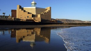 A coastal building with a prominent tower and a reflective water surface. - Stratus Loft Gran Canaria, elegance on Las Canteras beach. (Las Palmas de Gran Canaria)