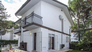 Un bâtiment à deux étages doté d’un balcon, d’un petit patio avec une table et des chaises, et d’une pelouse bien entretenue.