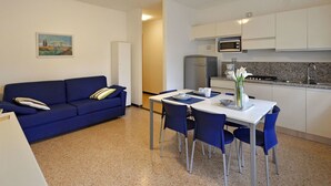 Un espacio habitable compacto con sofá, mesa de comedor, sillas, y una zona de cocina con refrigerador, microondas y lavaplatos.