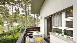 Un balcón con mesa y sillas, plantas en macetas y vistas a árboles y follaje.