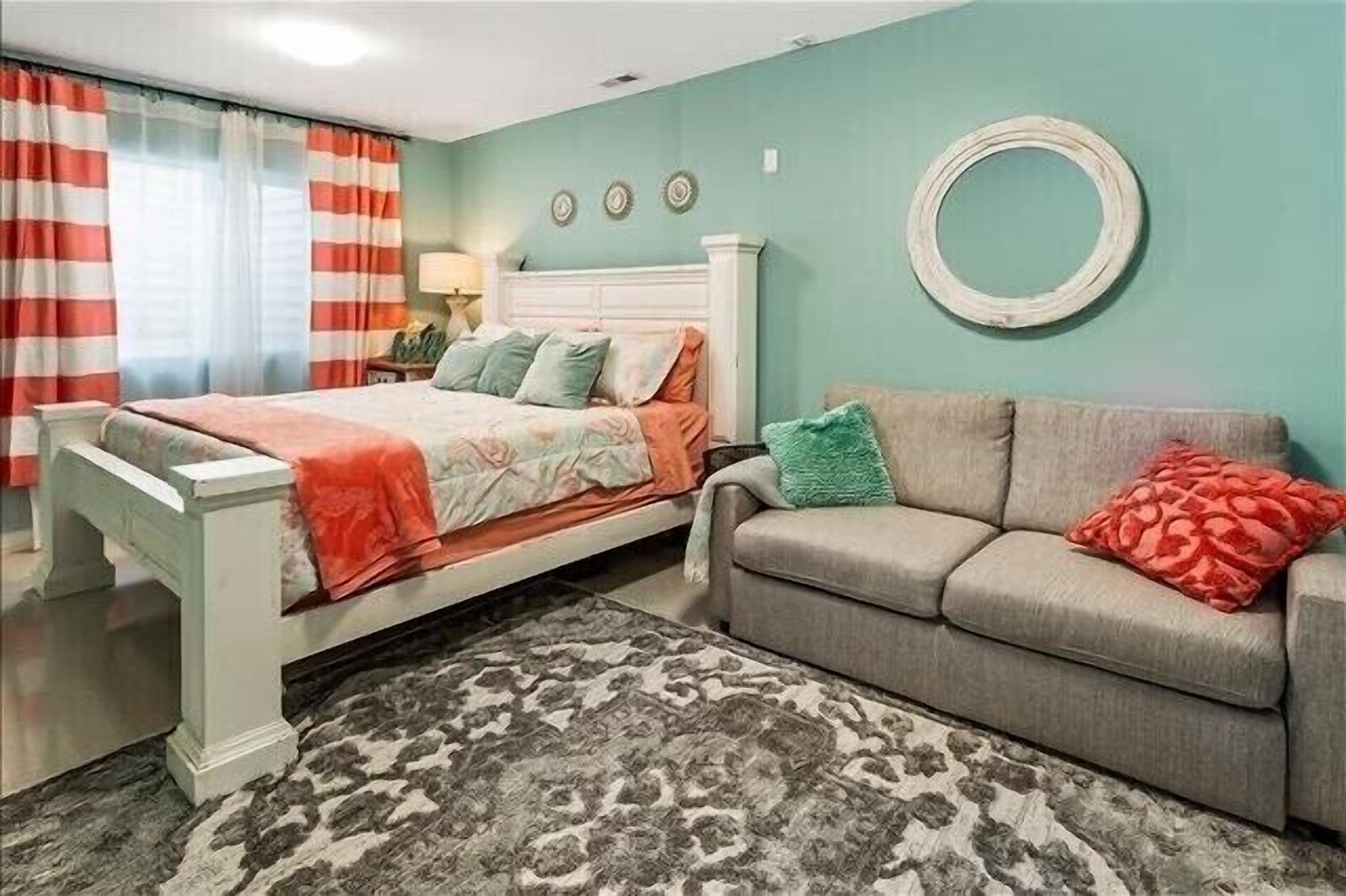 Ein Schlafzimmer mit einem Bett, einem grauen Sofa, einem gemusterten Teppich und einer türkisblauen Wand.
