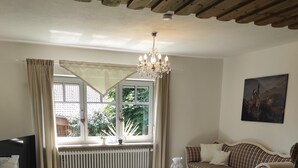A cozy living room with a wooden ceiling, a dining table with chairs, a sofa, and a painting on the wall.