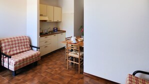 A compact kitchen with a dining area, a plaid sofa, and a small table with chairs.