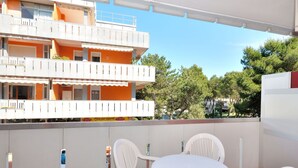 A balcony with a round table and chairs, overlooking a building with orange and white exterior walls.