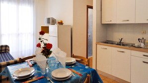 Een eethoek met een tafel gedekt voor twee, een keuken met witte kasten, en een koelkast met een magnetron erop.