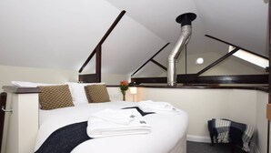 Ein Hotelzimmer mit einem großen Bett, einem Holzkopfstück, einem Deckenventil und einem kleinen Tisch mit einer Lampe.