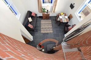 Et rum med højt til loftet, en spiralopsats, et spiseområde med et bord dækket til to personer, samt en siddeplads med en sofa og puder.