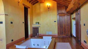 Ein geräumiges Zimmer mit einer großen Badewanne, Holzbalken an der Decke und zwei Wandleuchten.