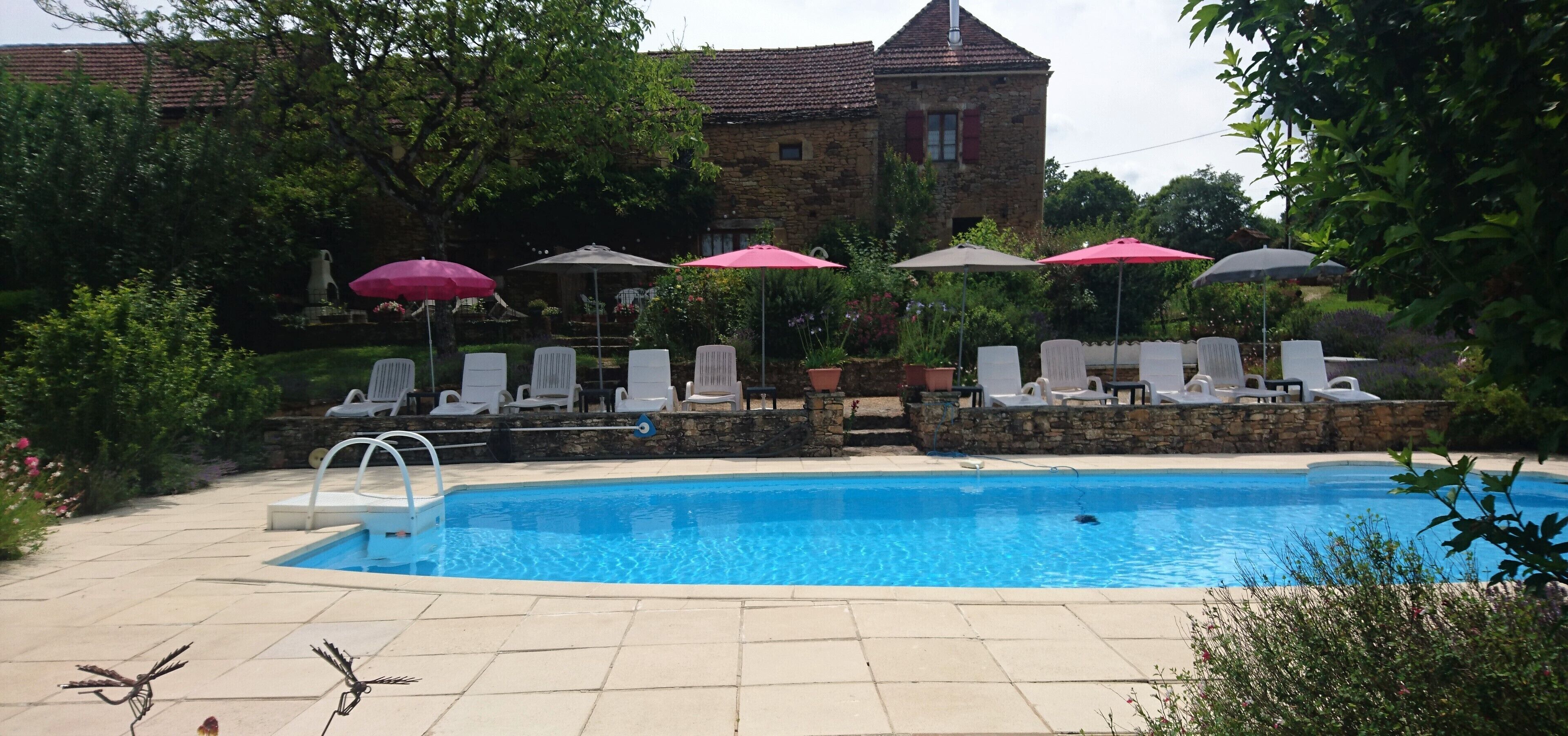A swimming pool with lounge chairs and umbrellas, surrounded by stone walls and greenery.