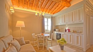 Una sala de estar acogedora con sofá, una mesa de comedor con sillas, una mesa de centro con un jarrón de flores y una cocina con armarios blancos y techo de madera.