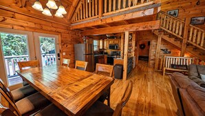Ein Holzblockhaus-Interieur mit Esstisch, Stühlen, einer Küchenzeile und einer Treppe.