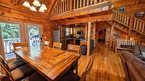 A wooden cabin interior with a dining table, chairs, a kitchen area, and a staircase.