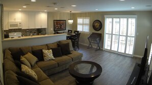 A spacious living area with a sofa, a coffee table, and a dining table with chairs. There is a kitchen area with cabinets and a microwave.