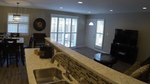 A modern kitchen with a large island, a dining area with chairs, and a living room with a TV.