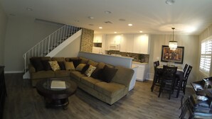 A modern living room with a sectional sofa, a coffee table, and a dining area with a chandelier.