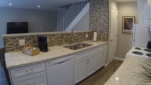 A modern kitchen with a granite countertop, stainless steel sink, white cabinetry, and a patterned backsplash.